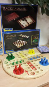 Spiel: Mensch-ärgere-dich-nicht in Holzausführung, dahinter verschiedene Spieleschachteln