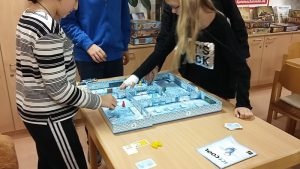 Bild: 3 Spieler stehen an einem Tisch um ein Spielfeld