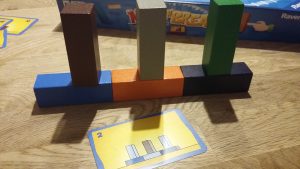 Bild: Karten mit Aufgabenstellung, dahinter gebautes Holzklotz-Gebäude