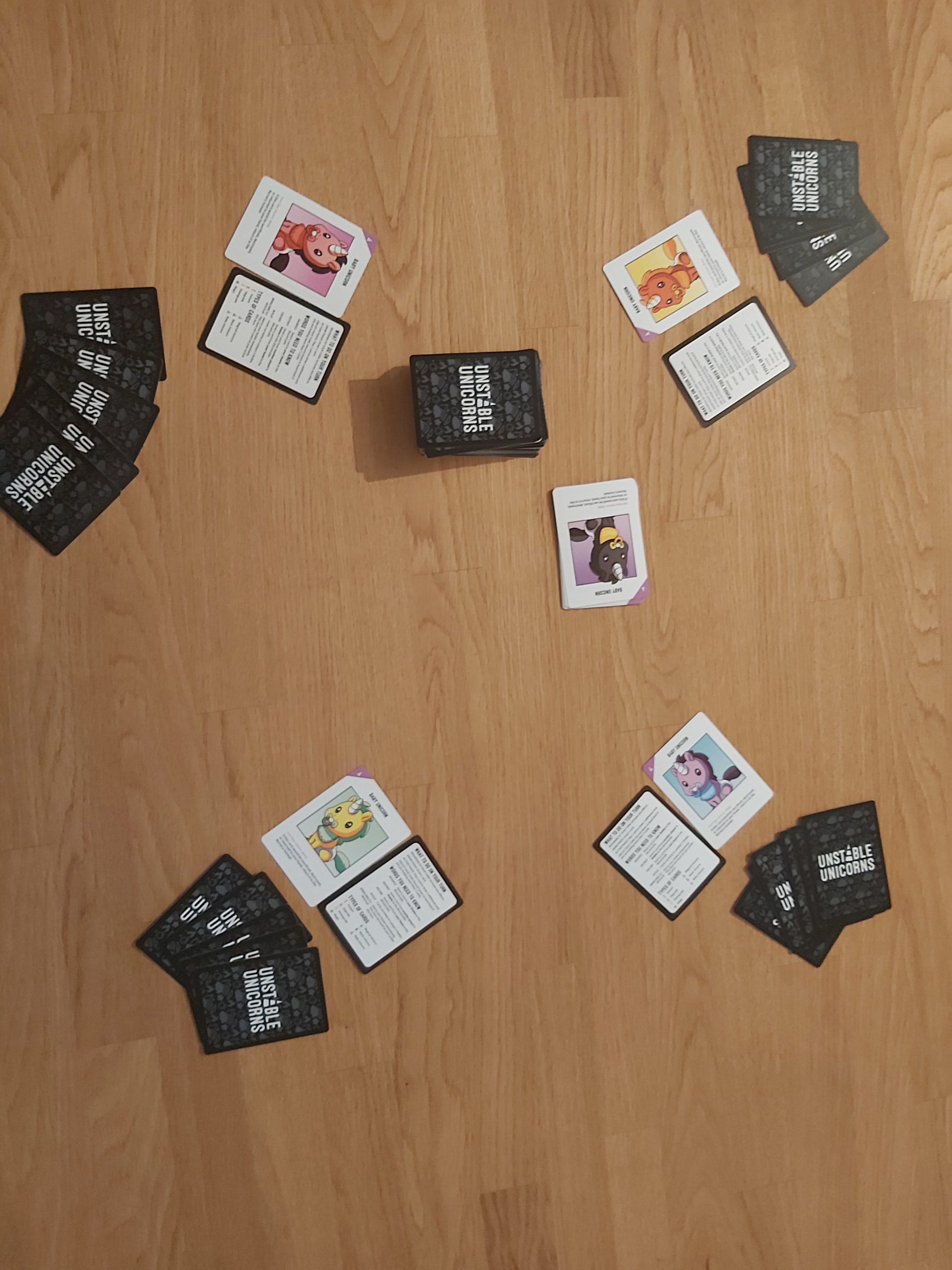 Zu sehen ist der Spielaufbau von Unstable Unicorns für 4 Spielende