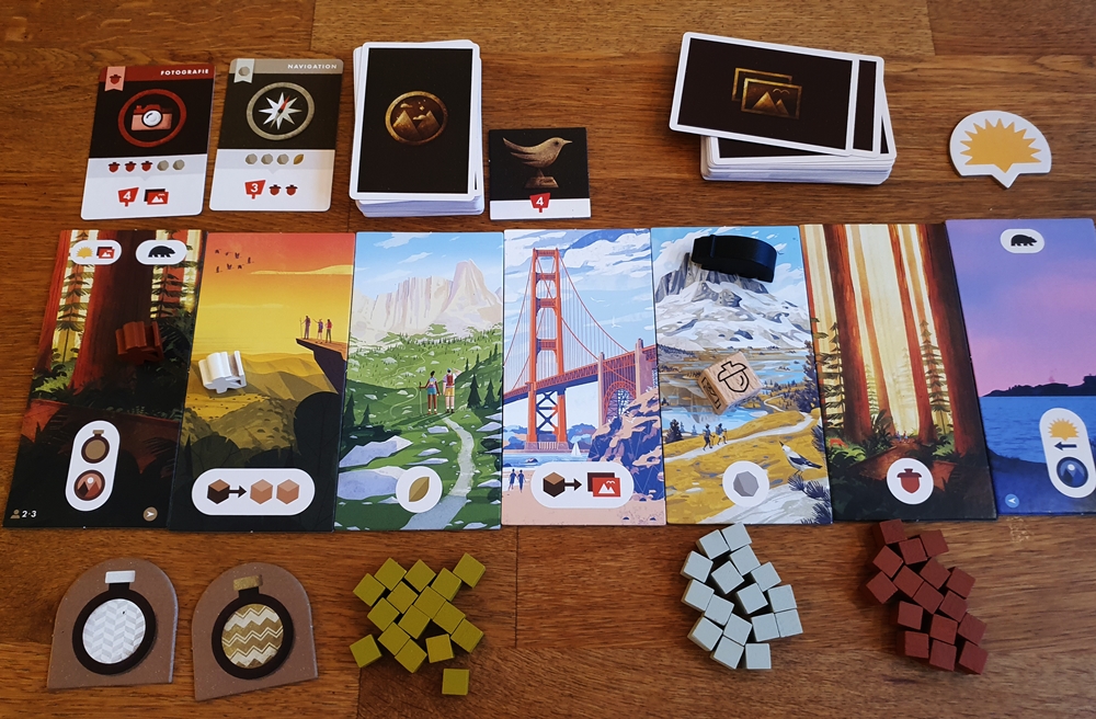 Der Aufbau zum Start: der Weg bestehend aus nebeneinander liegenden Teilen. Darunter Ressourcenplättchen, oben Auftrags- und Fotokarten