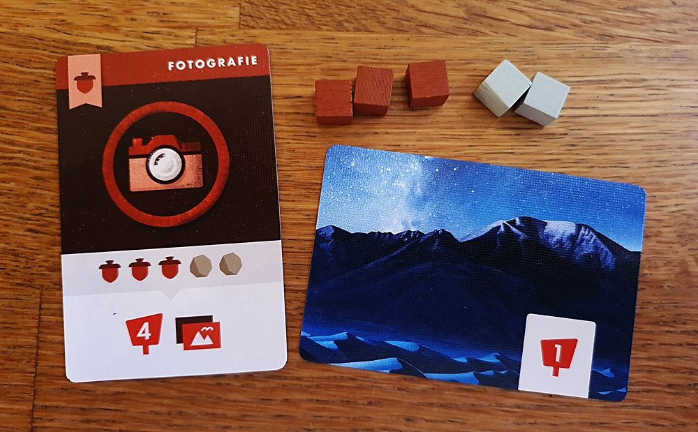 Eine Karte "Auszeichnung", die Ressourcenwürfel, mit denen man sie erfüllt, eine Fotokarte