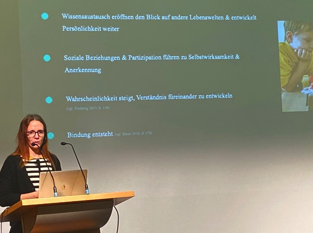 Petra vor einem Rednerpult, im Hintergrund eine Präsentation