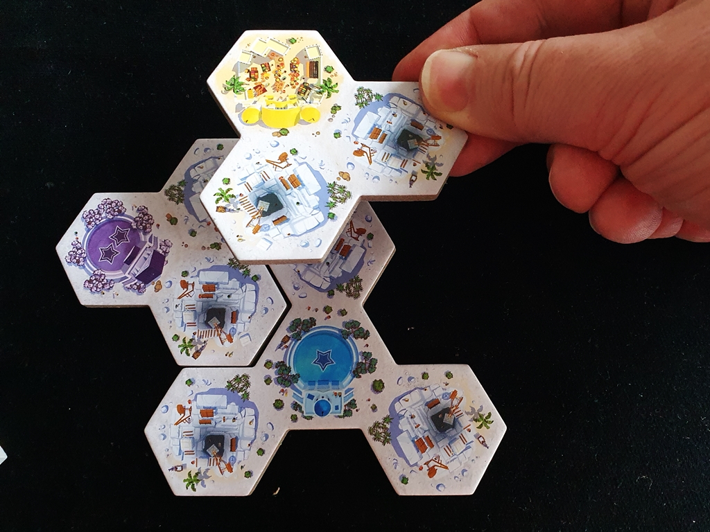 Hand, die ein Legeplättchen beim Überbauen in der eigenen Spielauslage zeigt