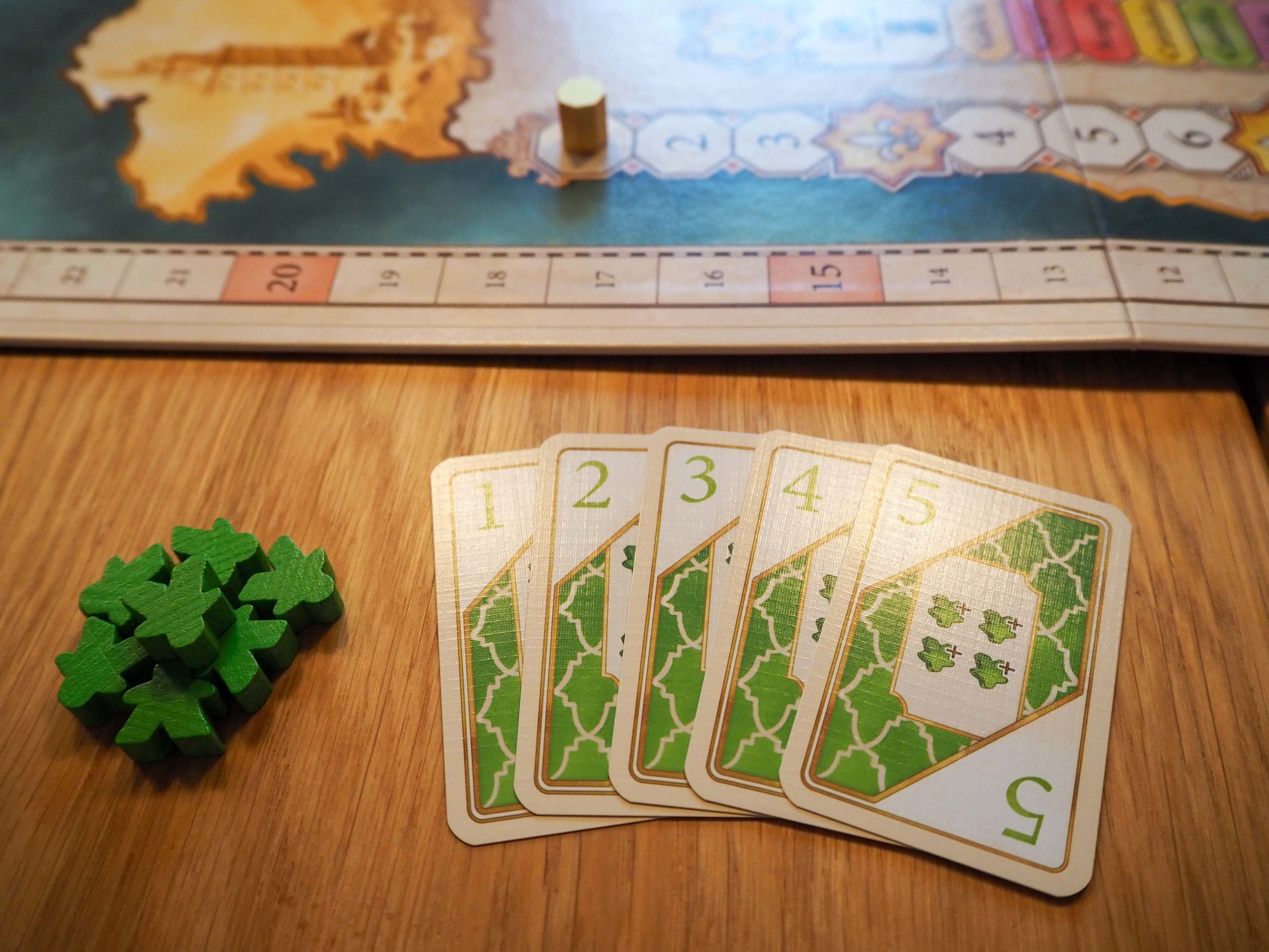 Im oberen Drittel liegt der Spielplan auf dem ein goldener Rundenanzeiger platziert ist. Im Vordergrund ist ein kleiner Haufen mit grünen Spielfiguren zu sehen. Rechts davon liegen aufgefächert, von 1 bis 5 nummeriert, so genannte Machtkarten. In der linken oberen und rechten unteren Ecke sind grüne Zahlen aufgedruckt. Mittig auf der obersten Karte sind außerdem vier grüne Spielfiguren zu sehen.