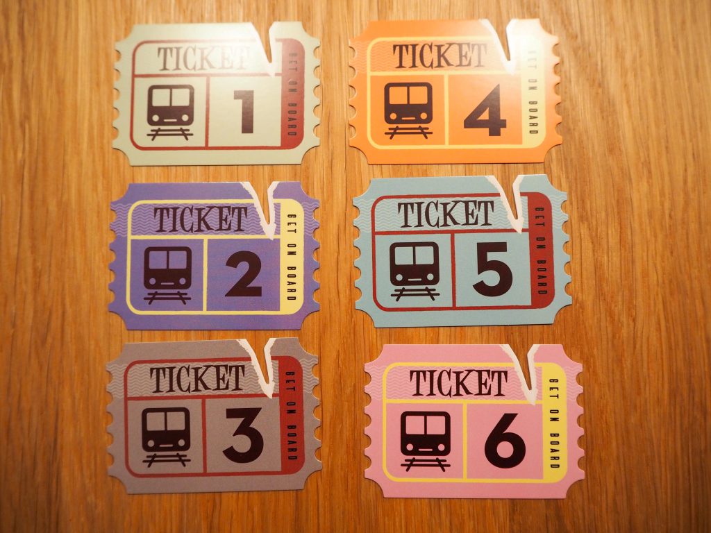Sechs Bahntickets in unterschiedlichen Farben in zwei Spalten, jeweils drei untereinander, liegen auf einem Holztisch.