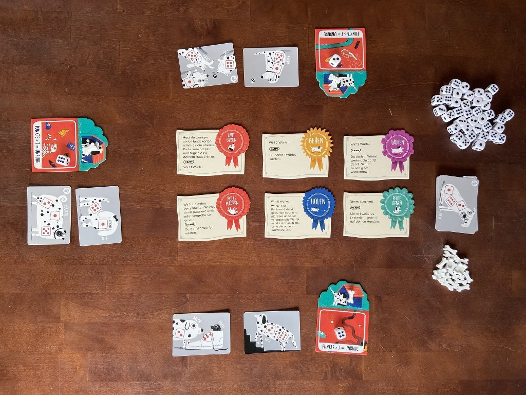 In der Mitte liegen 6 Karten mit Tricks. Für die Spielenden leigen jeweils ein Kartentableau und 2 Hundekarten bereit.