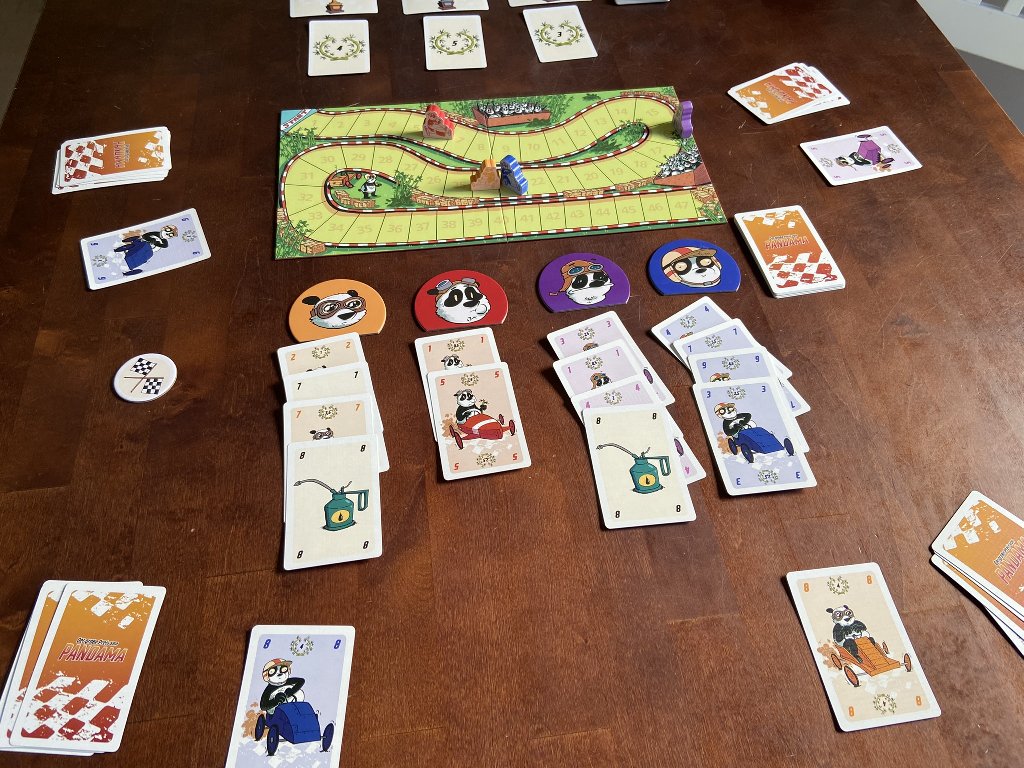 Der Spielplan liegt in der Mitte des Tisches. Drumherum sind Karten verteilt, vorne angeordnet in Reihen unter Pandamakern.