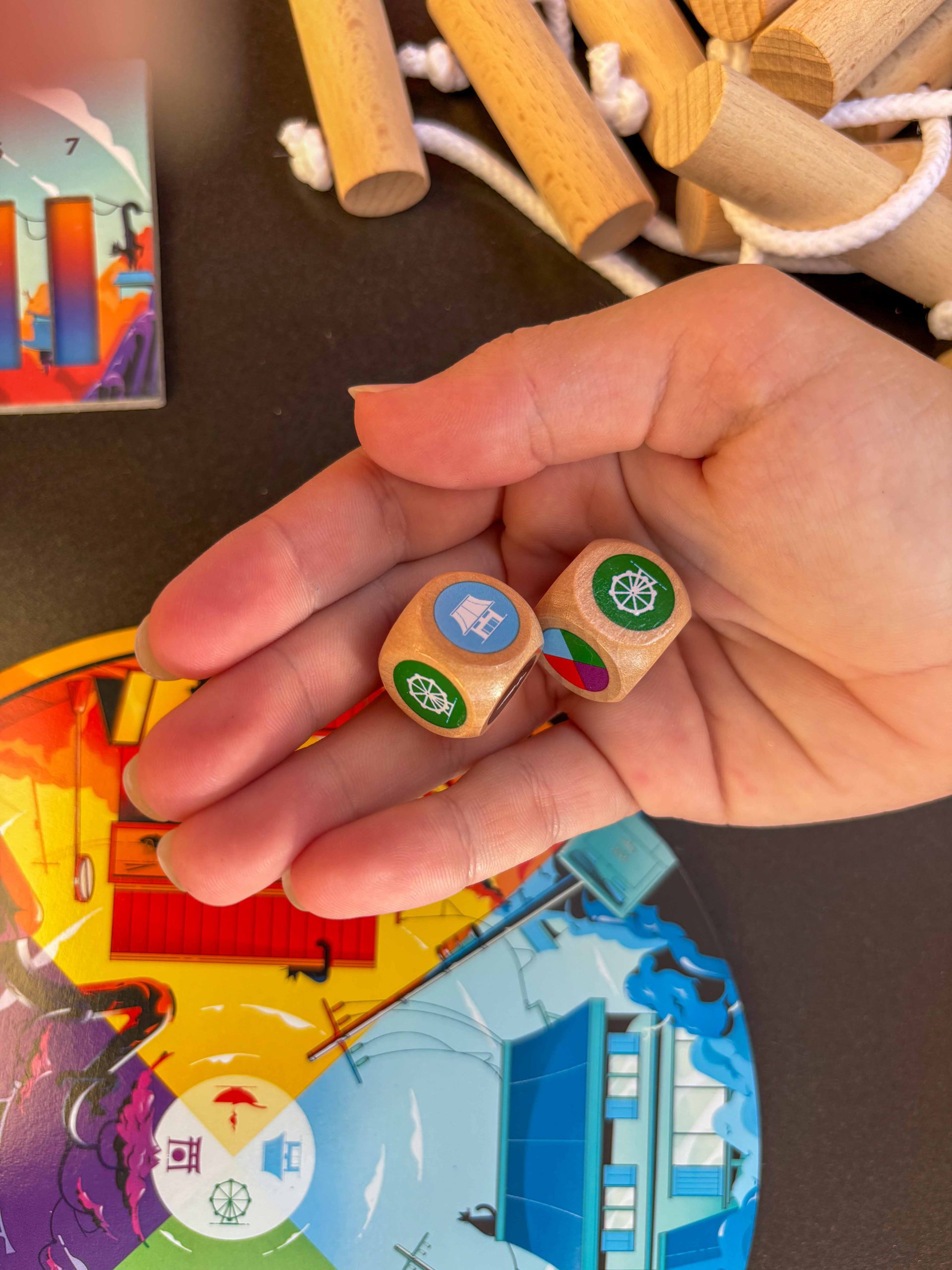 Zwei Würfel liegen in Kinderhand. Im Hintergrund verschiedenes Spielmaterial.