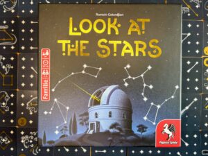 Look at the stars Spielschachtel und im Hintergrund schwarze quadratische Karten mit weißen Sternen und Strichen