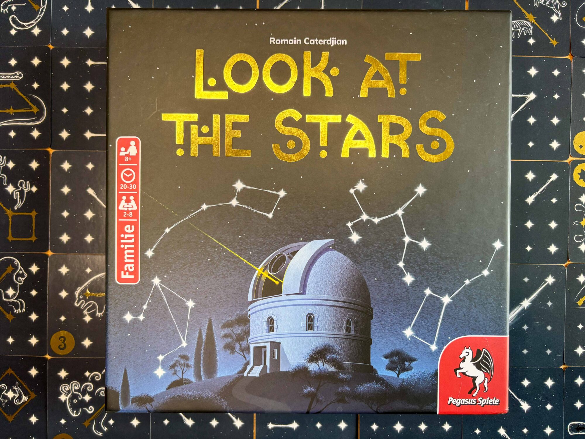 Look at the stars Spielschachtel und im Hintergrund schwarze quadratische Karten mit weißen Sternen und Strichen
